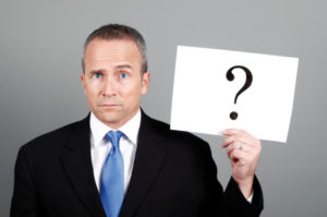 A man in a business suit and blue tie hold a sign with a questoin mark.